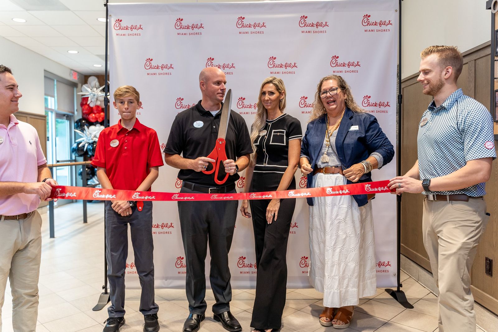 Ribbon cutting in front of a Chick-fil-A Miami Shores backdrop at the restaurant's grand opening